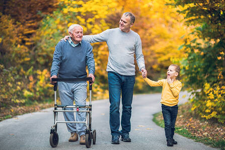 A man with a walker walking with a younger man and a child on a fall day
