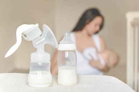 A breast pump and baby bottle partially filled with milk, and a nursing person and baby in the background